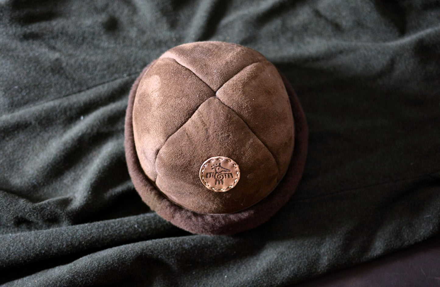 Vue de dessus du bonnet shearling mouton, détail des coutures artisanales et patch oiseau