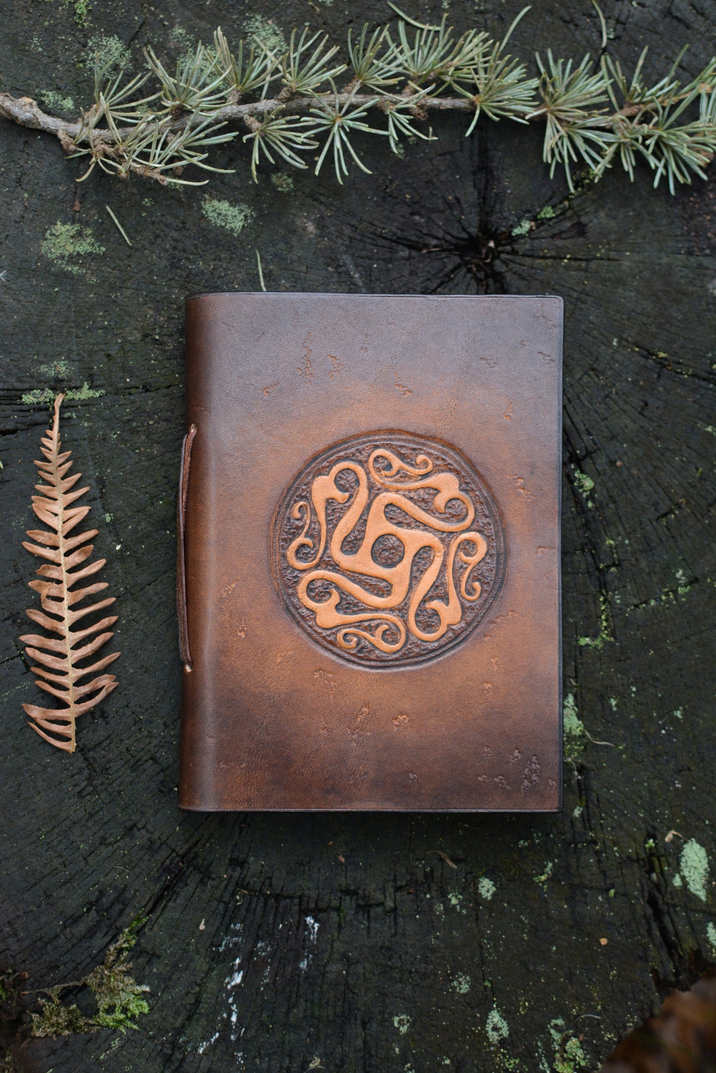 Carnet en cuir tannage végétal motif celte ancien vu de face posé sur une souche de bois - Amrod & Gardarson