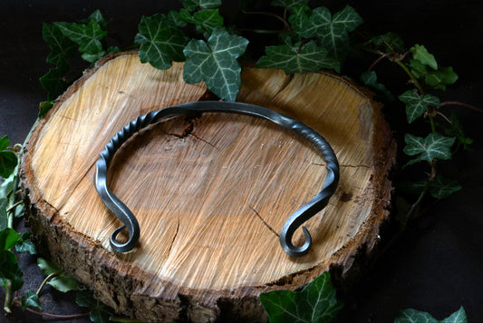 Collier torque en fer forgé présenté sur un rondin de bois et feuilles de lierre