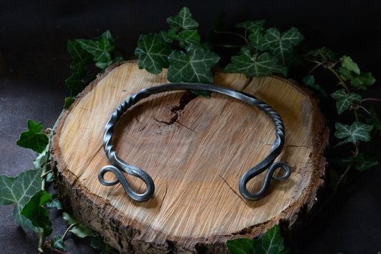 collier torque forgé présenté sur rondin de bois et feuilles de lierre