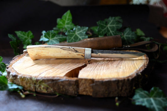 Couteau forgé avec manche en bois de cerf et hêtre échauffé posé sur un rondin en bois et décor feuilles de lierre