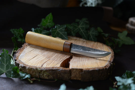 Couteau forgé avec manche en charme et noyer posé sur un rondin en bois avec décor feuilles de lierre
