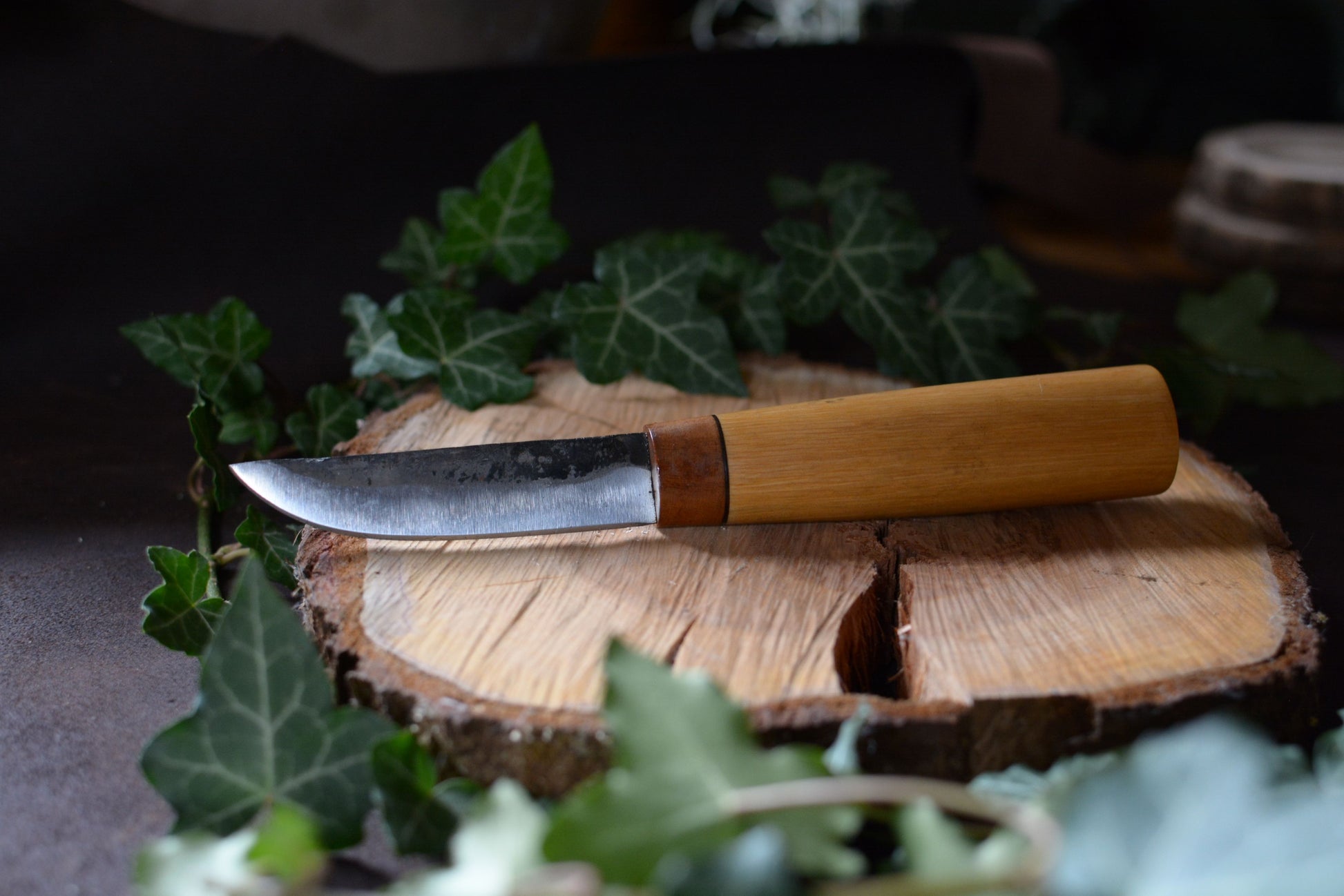 Couteau forgé avec manche en charme et noyer posé sur un rondin en bois avec décor feuilles de lierre