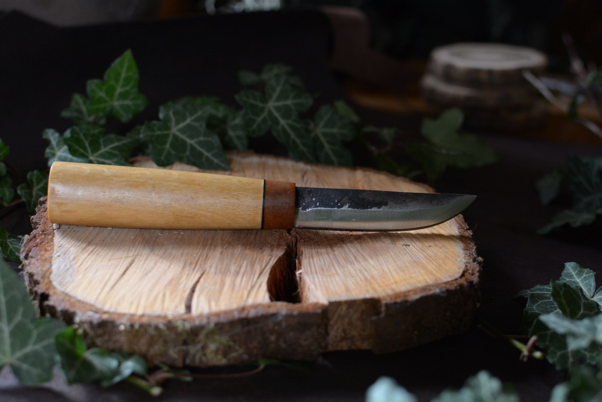 Couteau forgé avec manche en charme et noyer posé sur un rondin en bois avec décor feuilles de lierre