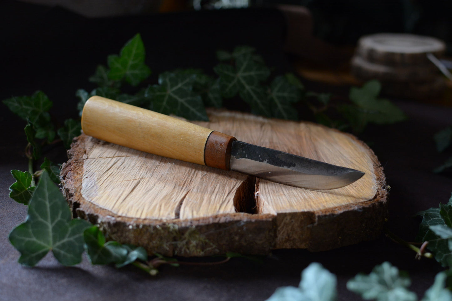 Couteau forgé avec manche en charme et noyer posé sur un rondin en bois avec décor feuilles de lierre