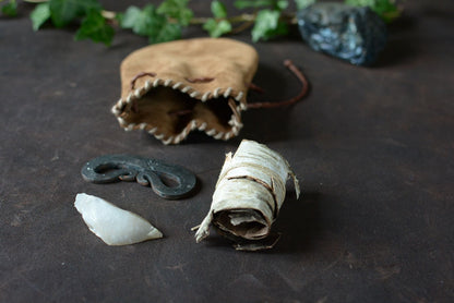 Kit allume-feu traditionnel avec bourse en cuir ouverte présentant le briquet, le silex et l'écorce de bouleau