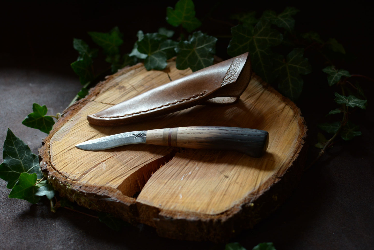 Petit couteau forgé main acier XC75 manche chêne brûlé buis padouk avec étui cuir sur-mesure - vue de face sur rondin de bois - Forge Gardarson
