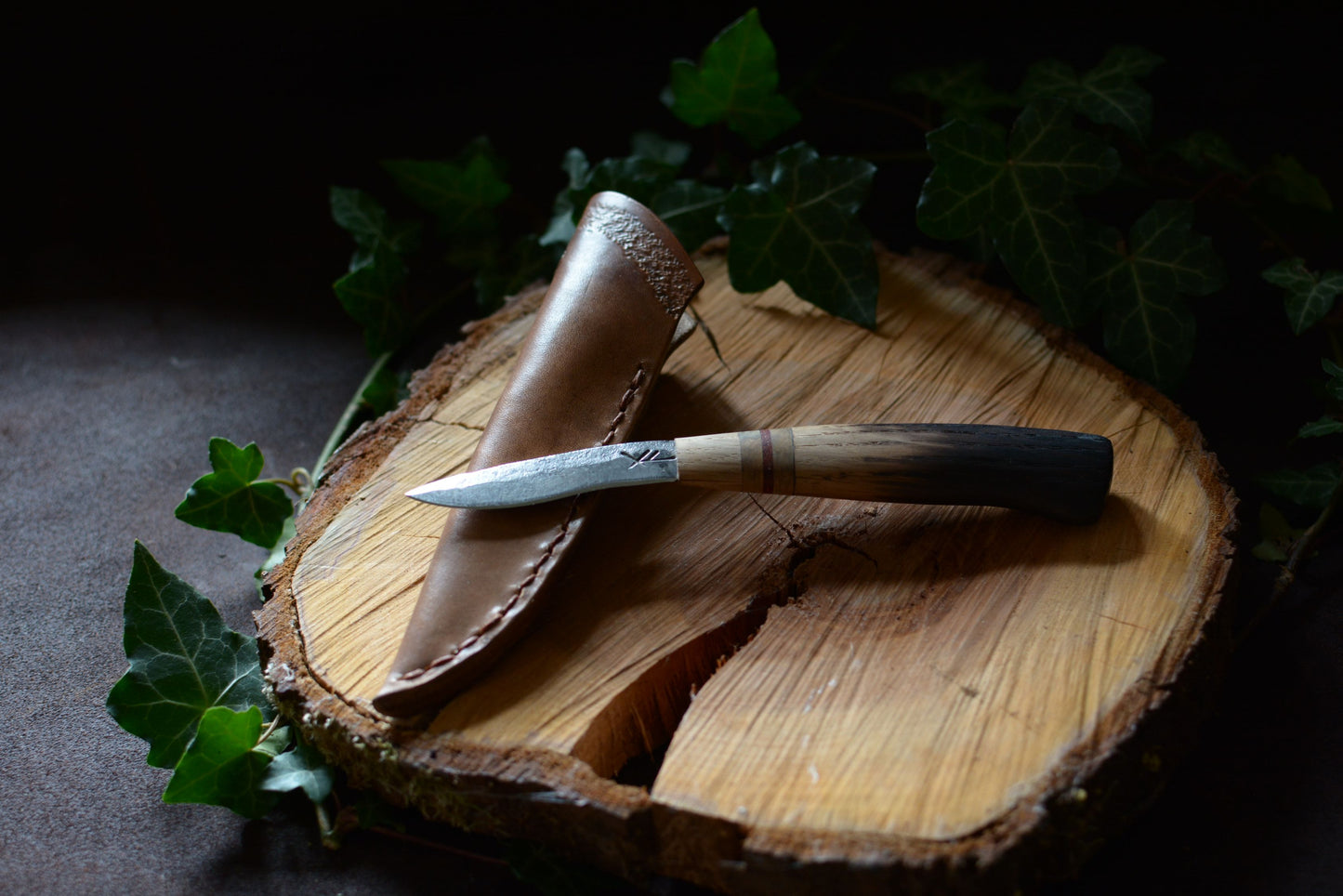 petit couteau en chêne brûlé avec son étui en cuir sur rondin en bois et feuilles de lierre