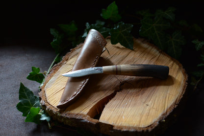 petit couteau en chêne brûlé avec son étui en cuir sur rondin en bois et feuilles de lierre